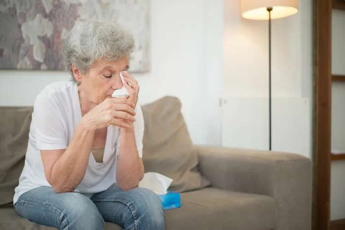 Older woman wiping tears sitting on couch reflecting on little time left
