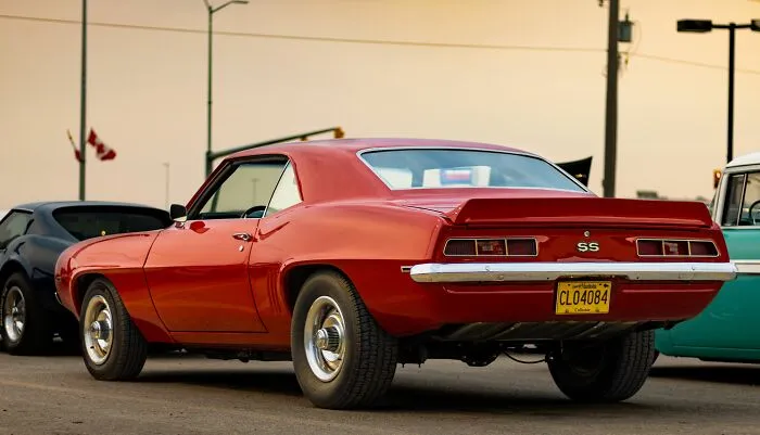 Red classic muscle car parked outside during sunset with vintage vehicle details
