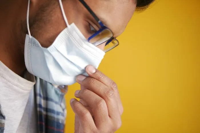 Man wearing mask and glasses touching nose against yellow background