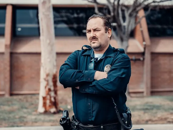 Thoughtful man in uniform standing with arms crossed outdoors