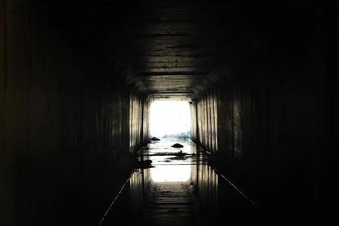 Dark tunnel with light at the end reflecting on water