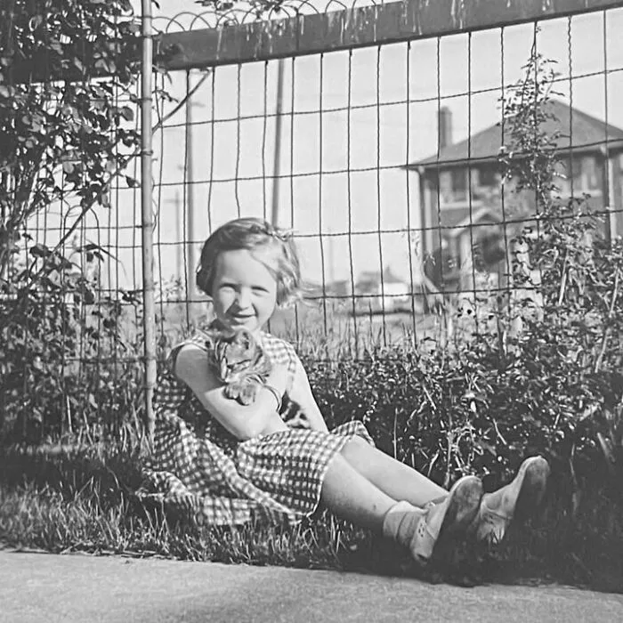 A young girl sits on the grass holding her kitten in vintage photos of children with their cats