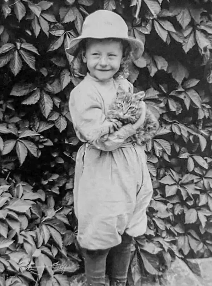 Vintage photo of a smiling little girl in a hat holding a fluffy tabby kitten