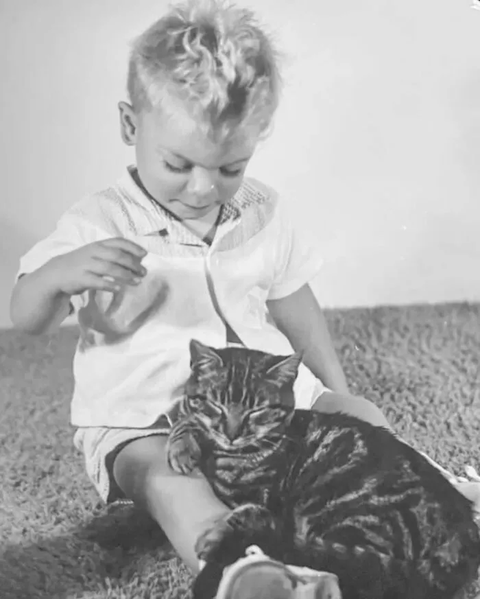 Vintage photo of a young boy looking down at a tabby cat sleeping on his lap