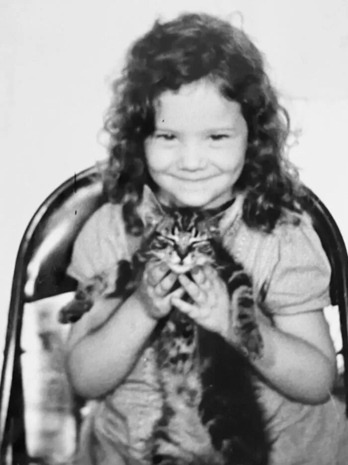 A cheerful girl cradles a small kitten in her arms from vintage photos of children with their cats