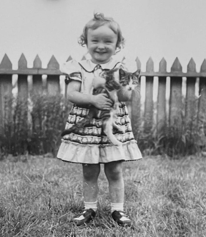 A smiling young girl in a dress holds a striped kitten in these vintage photos of children with their cats