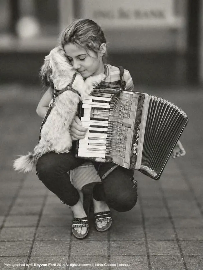 A black and white dog and cat photo of a girl hugging her dog while holding an accordion