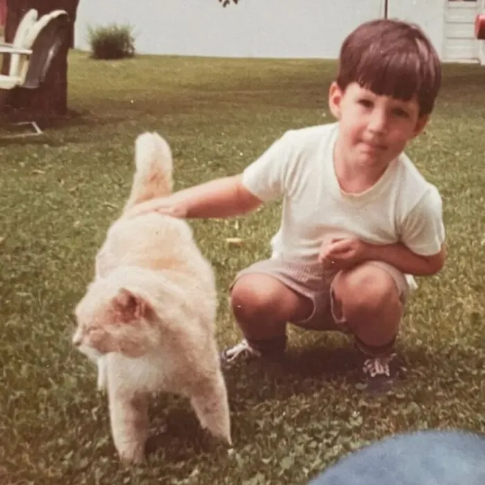A little boy crouches on the grass next to a cat in one of many vintage photos of children with their cats