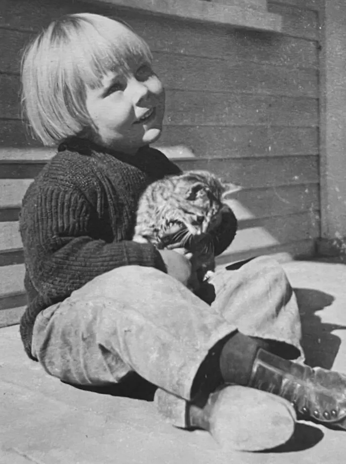 A young child sitting outside and cuddling a kitten, from vintage photos of children with their cats