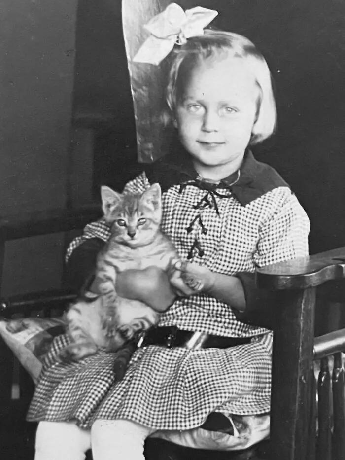 Little girl in a plaid dress holding a tabby kitten, part of vintage photos of children with their cats