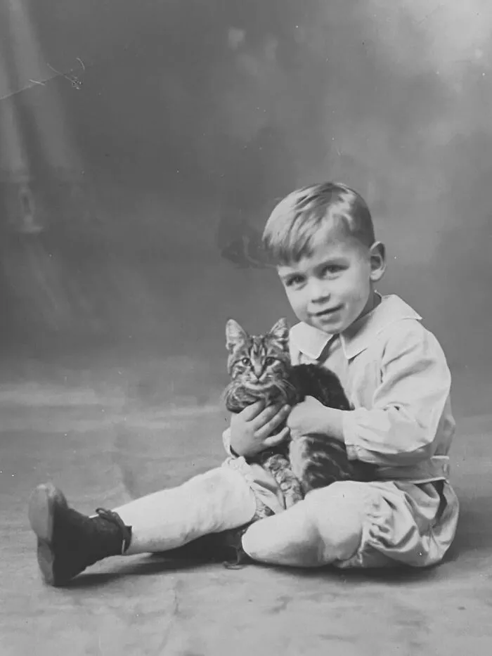 Young boy sitting on the floor holding a tabby cat, in vintage photos of children with their cats