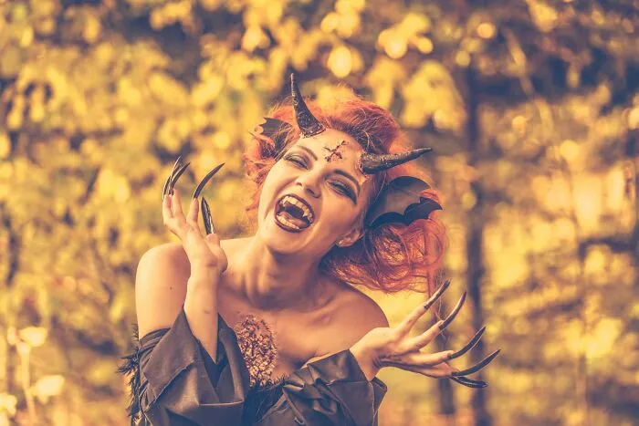 A woman wearing a scary demon costume with long black nails, reflecting dramatic Halloween conflicts in party attire.