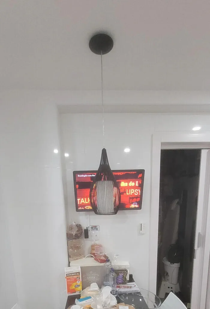 A modern black pendant light hanging unevenly in front of a wall-mounted TV during a home renovate attempt