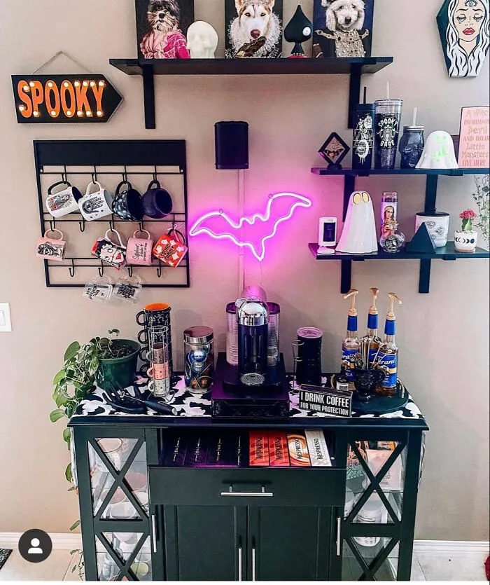 Coffee station decorated with spooky Halloween items including a pink neon bat light.
