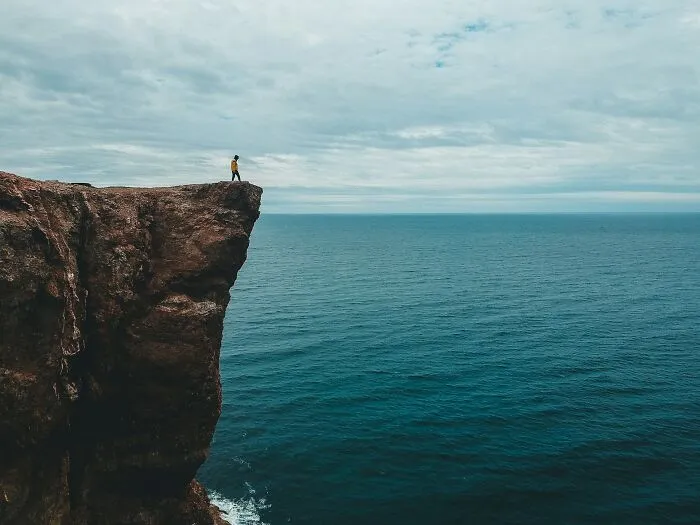 A person standing on the edge of a high cliff looking over the ocean, reminiscent of a dramatic Hollywood scene.