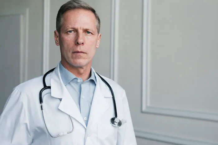 Serious male doctor in a white coat with a stethoscope looking sternly at the camera