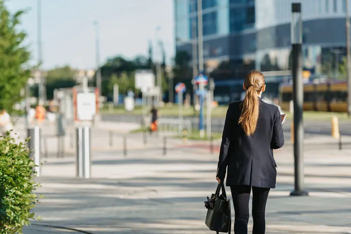 Professional woman carrying a handbag walking outside near office buildings