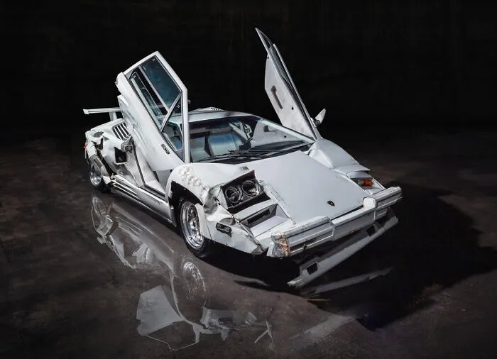 A damaged white Lamborghini Countach used as movie props on a dark showroom floor.