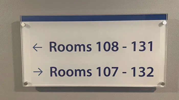 A directional wall sign pointing to overlapping room numbers, one of many absurd signs and moments.