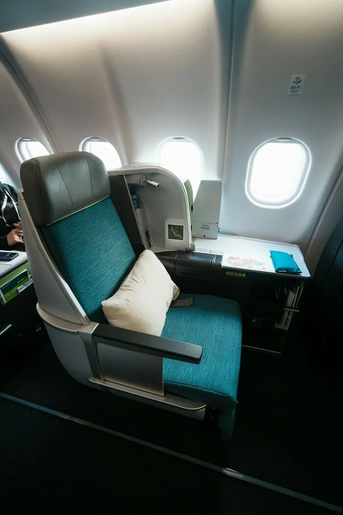 An empty business class seat with a pillow inside airplane cabin