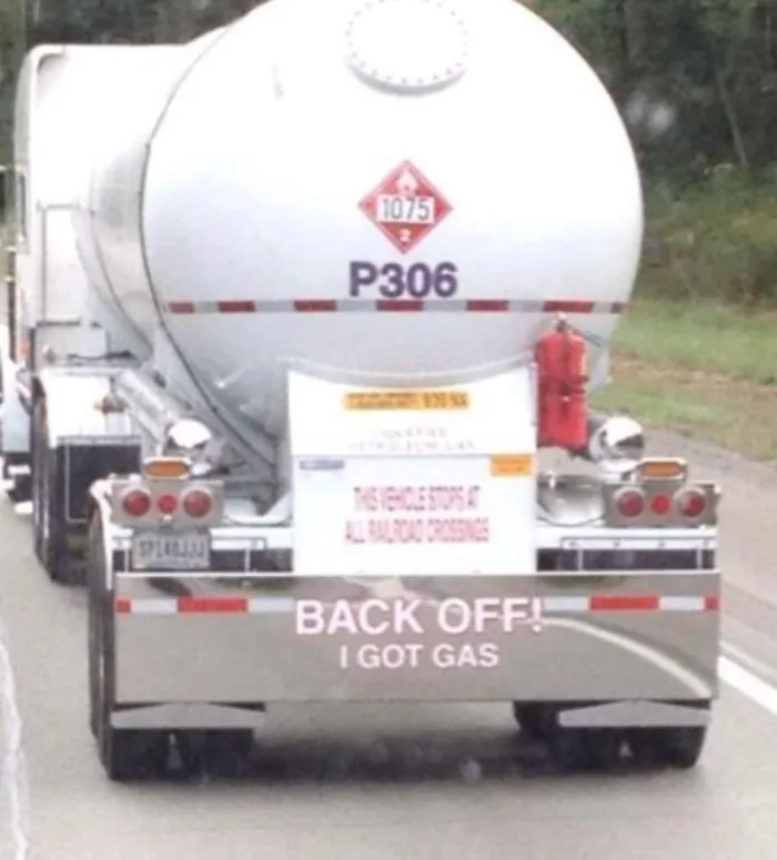 Rear of a white gas tanker truck with a funny message reading BACK OFF! I GOT GAS.
