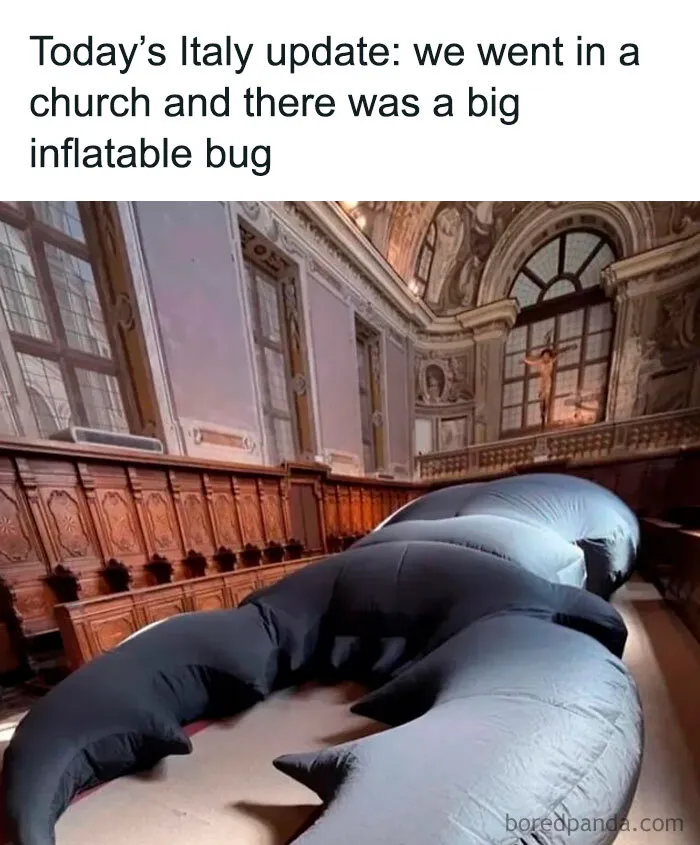 Large black inflatable insect sculpture lying in a church hall, funny weird animal memes