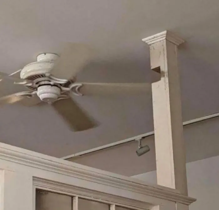 A white ceiling fan with a blade going through a cutout in a pillar, showing bad home renovation choices.