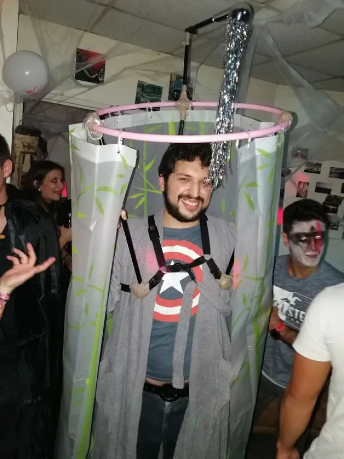 A man wearing a homemade shower stall contraption as a unique Halloween costume idea at a party.