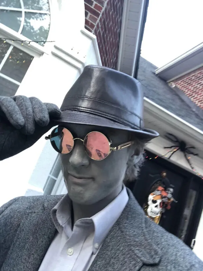 A man in grey makeup, hat, and sunglasses posing as a black and white film character for Halloween costume ideas.