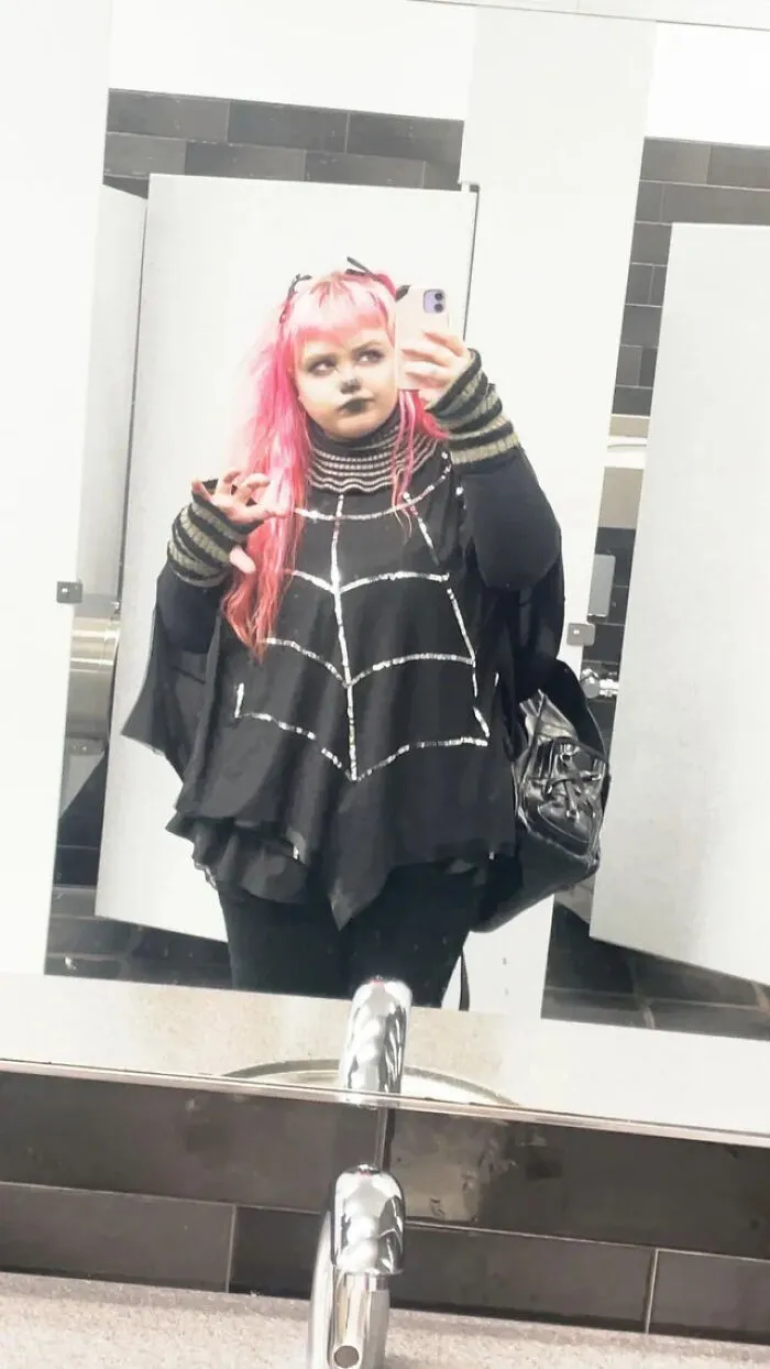 Person with pink hair in a spiderweb outfit posing for Halloween costume ideas.