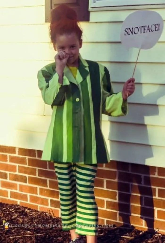 Young girl in a green striped outfit holding a speech bubble sign, showing unique Halloween costume ideas.