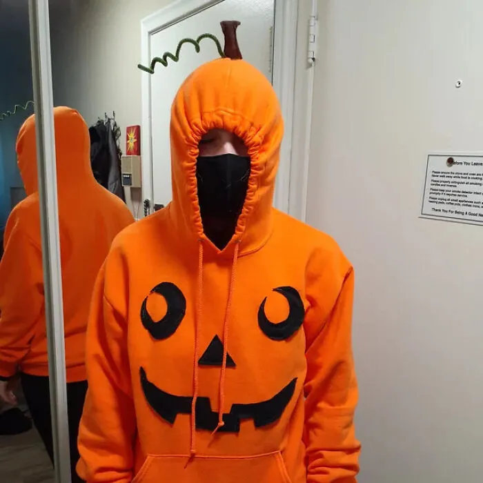Person wearing an orange pumpkin hoodie with a jack-o-lantern face as an easy, last-minute Halloween costume idea.