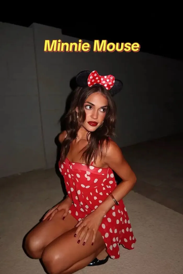 A woman posing in a red polka dot dress and mouse ears for a Minnie Mouse Halloween costume idea.