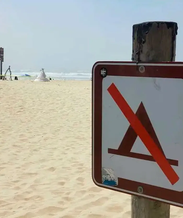 A sign prohibiting tents on a beach with an actual tent visible in the background