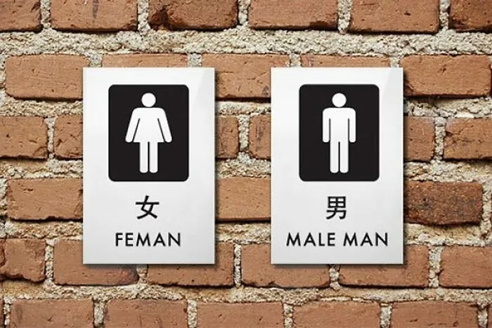 Restroom signs showing translation fails with FEMAN and MALE MAN written on a brick wall.