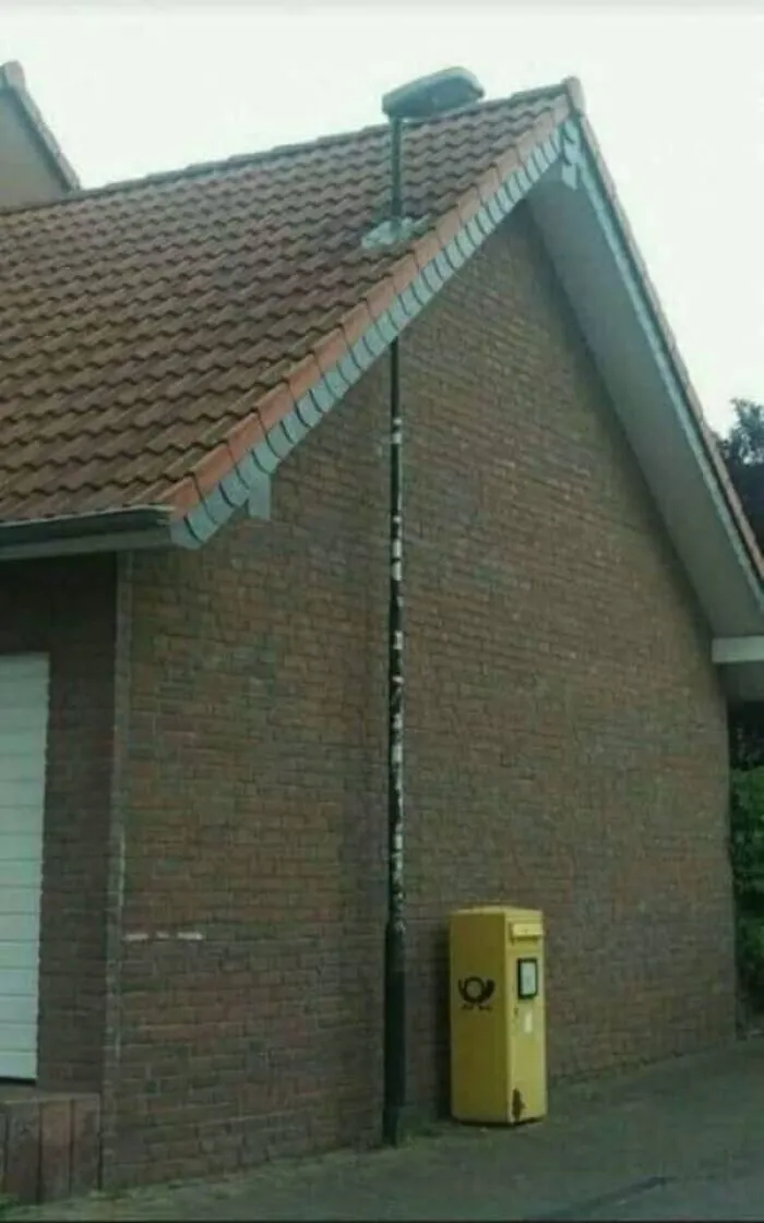 A streetlight installed straight through the roof edge of a brick house, depicting odd Slavic engineering.