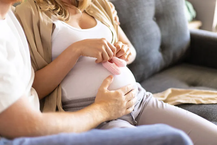 An expectant mother and her partner holding pink baby booties over her pregnant belly.