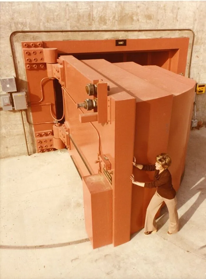 A woman pushing an incredibly massive and heavy steel door, showing an entertaining pic of a giant vault