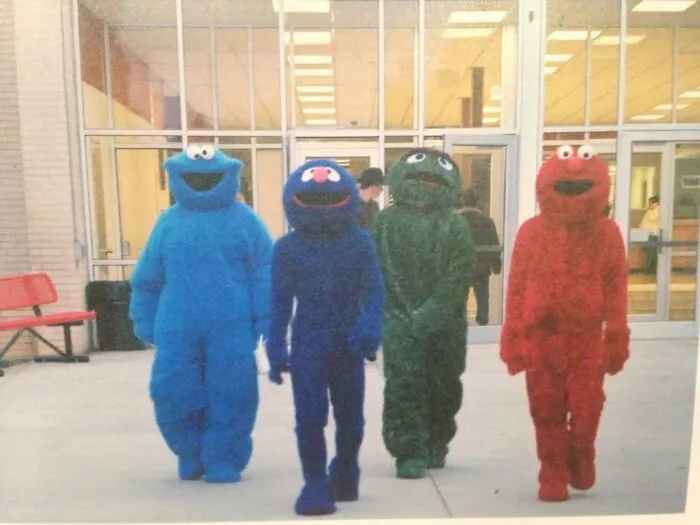 Four people dressed in Sesame Street mascot suits outside a building, showcasing fun creative Halloween costume ideas.