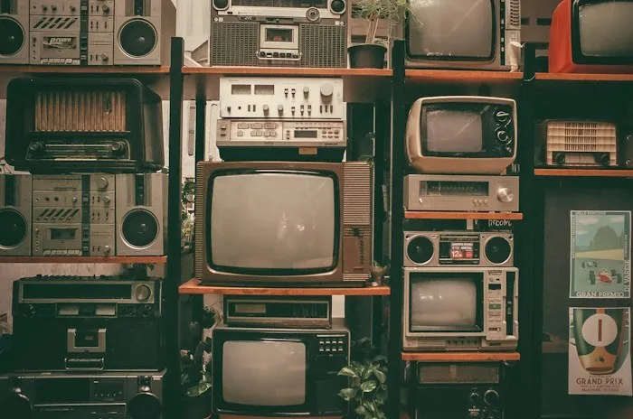 A wall shelf filled with vintage televisions and radios, an example of unique dumpster finds.