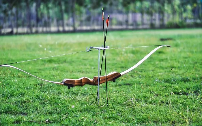 An archery bow resting on a metal stand outdoors in a grass field, showcasing wild dumpster finds.