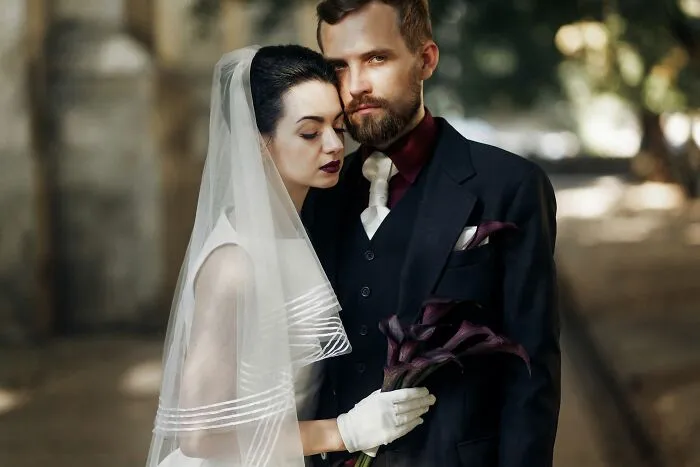 A couple dressed in dark wedding attire posing together, fitting scary Halloween themes.