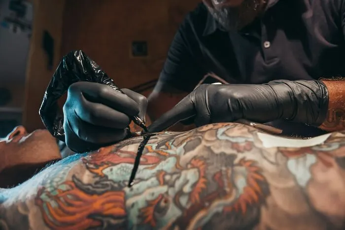 A tattoo artist working on a client, reminding of relationship fights concerning tattoos.