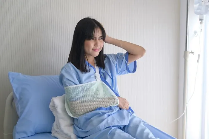 A female patient with an arm sling sitting in a hospital bed after professionals made clients lose trust