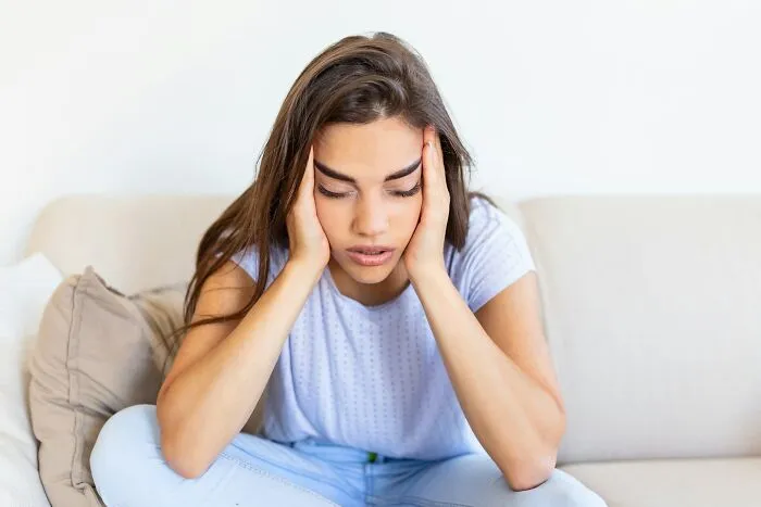 A woman sitting on a couch with her hands on her head looking stressed, depicting women's bodies and health misconceptions.