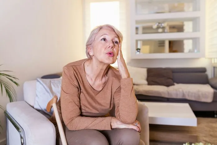 A senior woman sitting thoughtfully indoors, representing Halloween conflicts over family situations.
