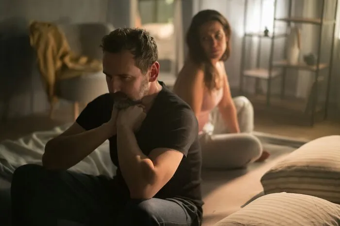 Sad couple sitting in a dim room after painful infidelity stories unfold in their relationship.