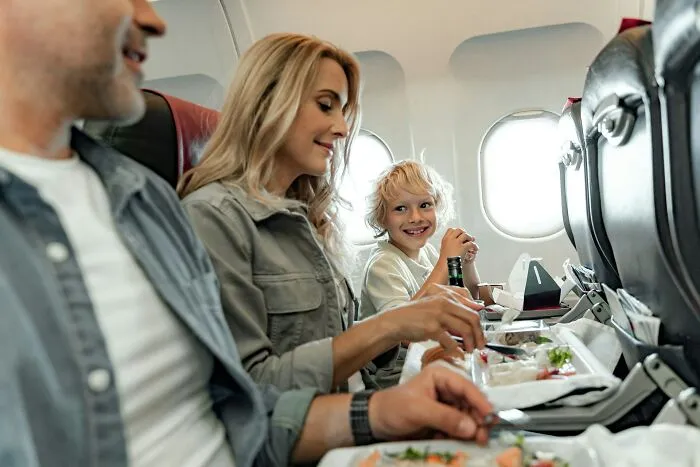 A family with kids sits in their seats on a plane enjoying a meal together