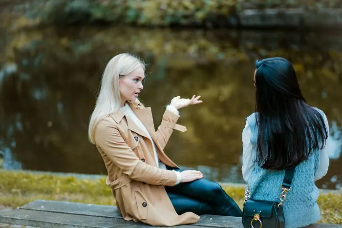 Two women sitting on a bench by the water discussing behaviors they do not tolerate