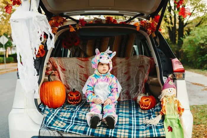 A toddler wearing a unicorn costume sitting in a decorated car trunk for trunk or treat Halloween